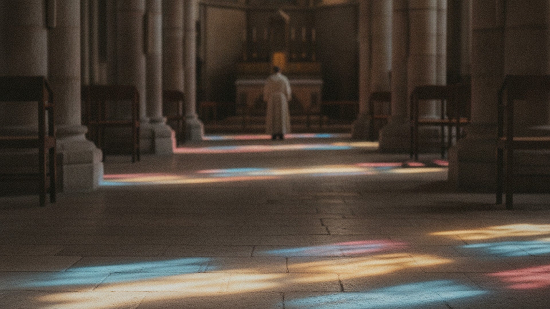 Lumière colorée d'un vitrail projetée en taches rouges, bleues et dorées sur le sol de pierre d'une nef vide