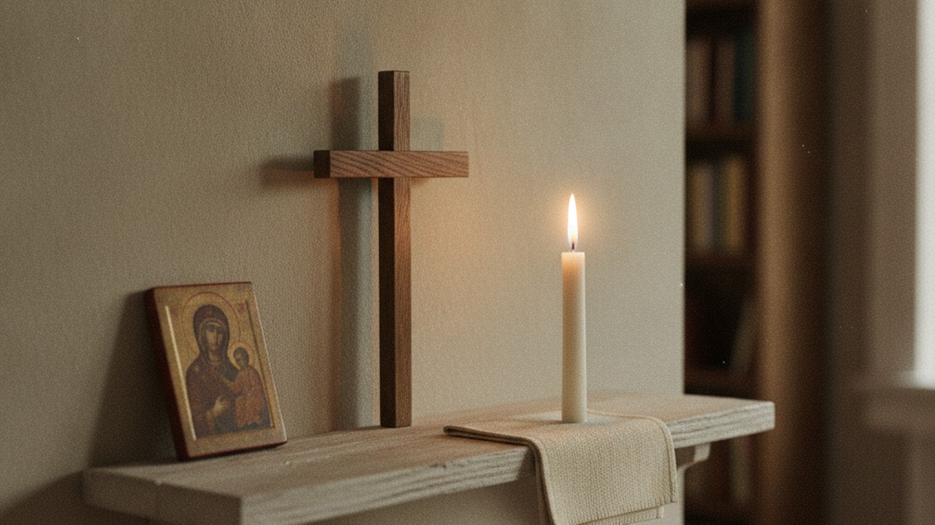 Coin prière domestique sur une étagère de bois : crucifix simple, bougie allumée, linge plié et petite icône
