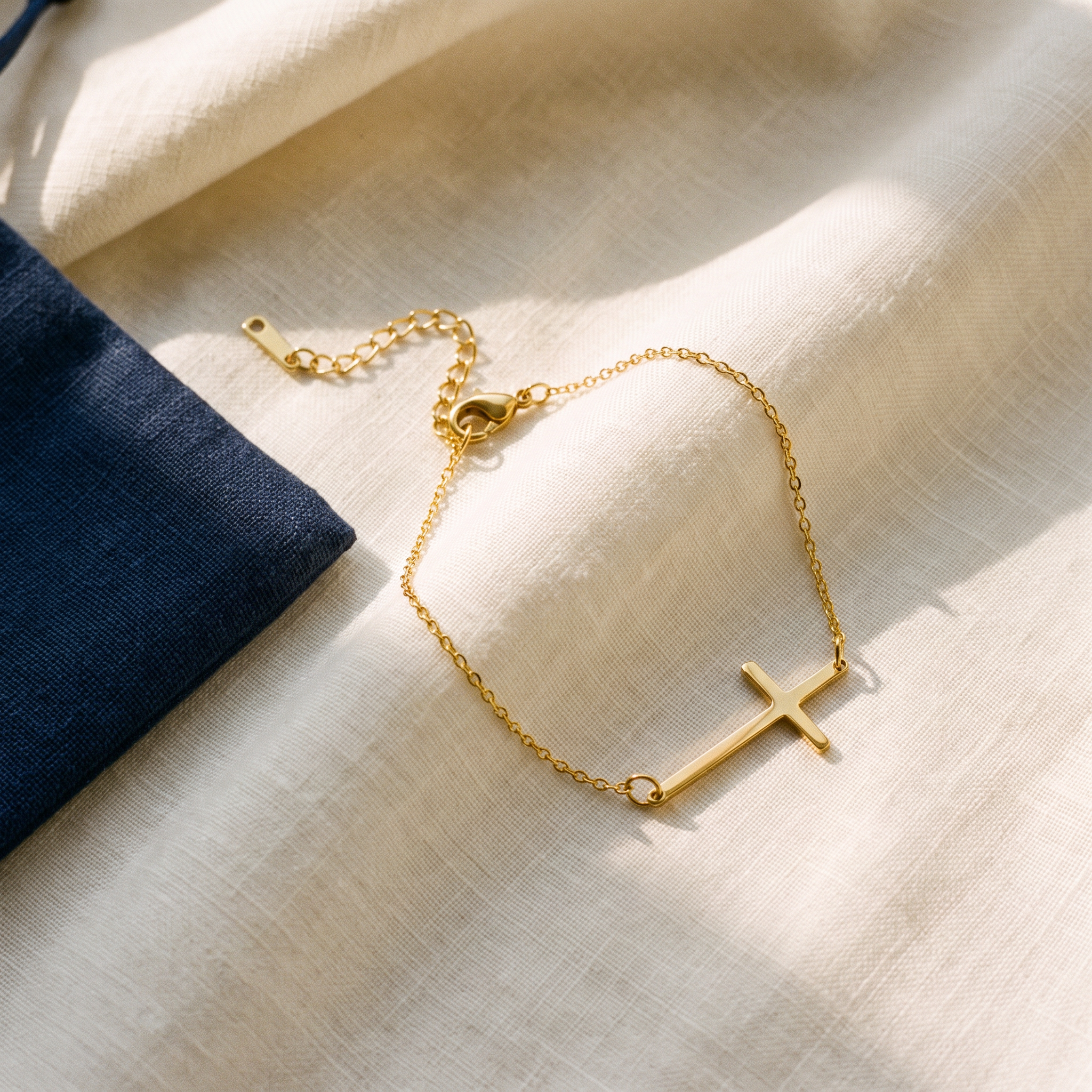 Bracelet croix minimaliste - Zita posé sur du lin ivoire, pochon marine en accent