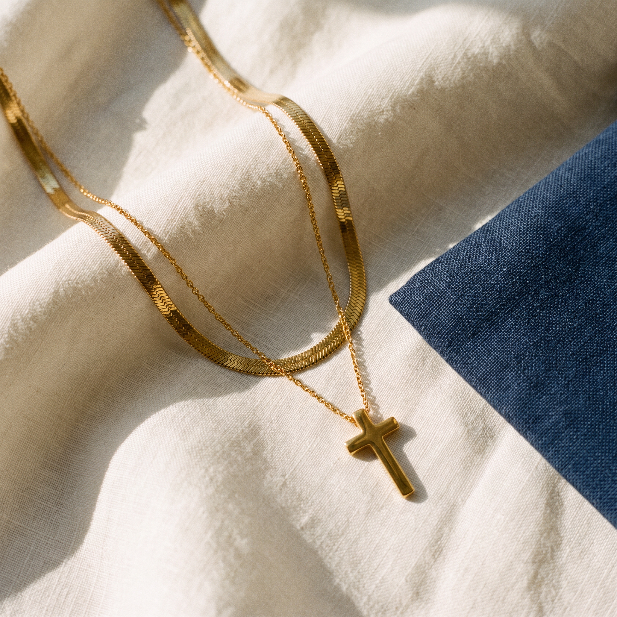Collier croix double chaine - Émeline posé sur du lin ivoire, pochon marine en accent