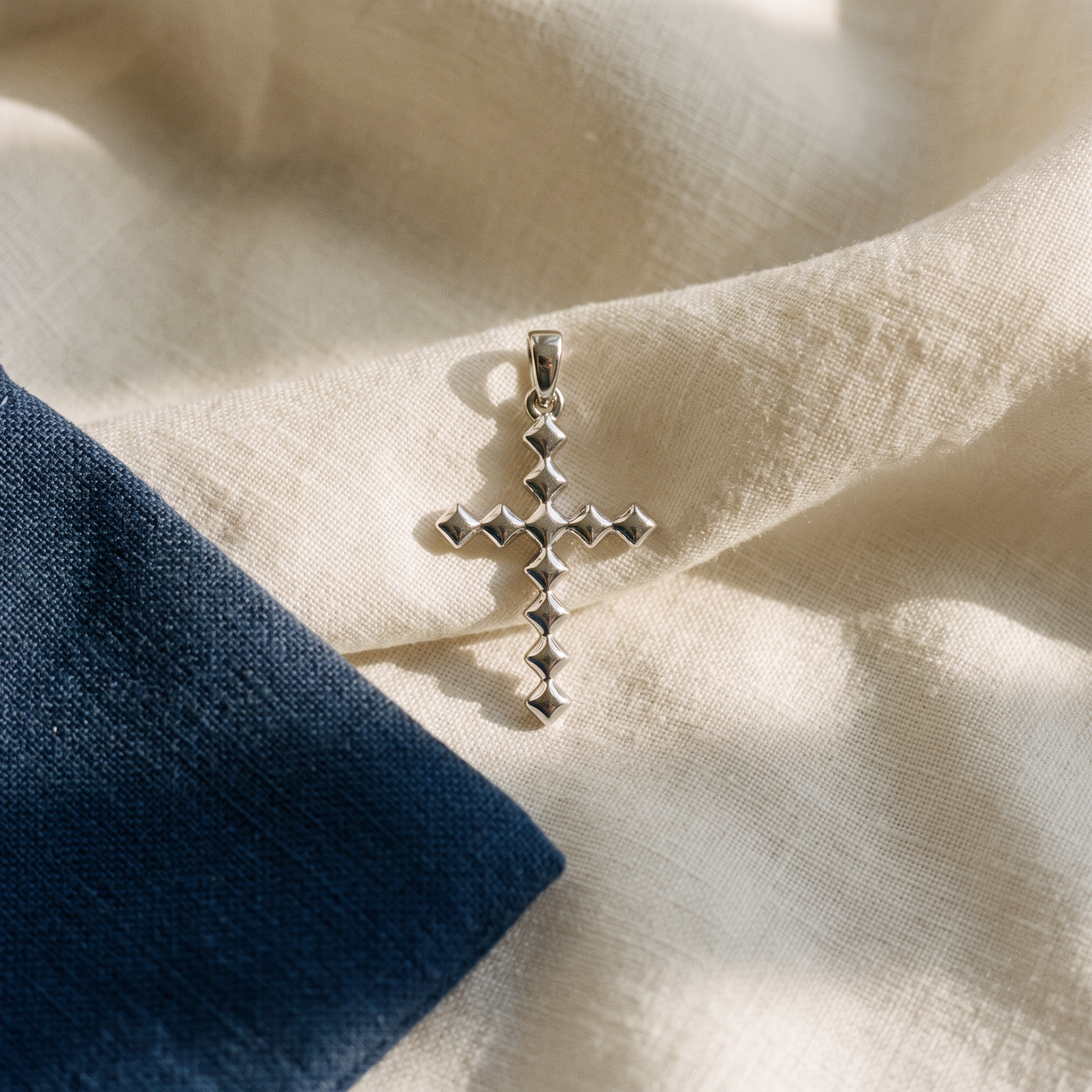 Pendentif croix femme argent posé sur du lin ivoire, pochon marine en accent