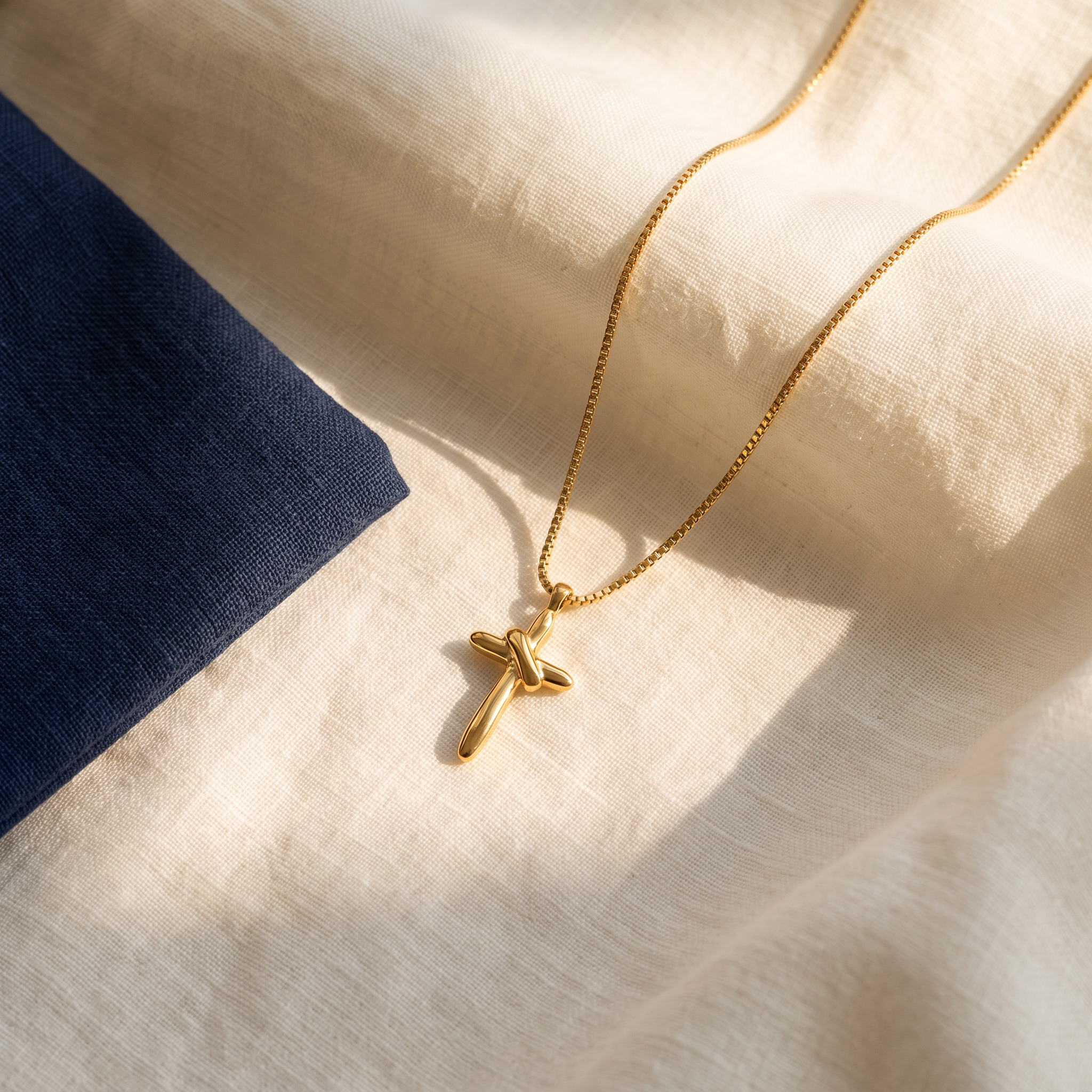 Pendentif croix religieuse posé sur du lin ivoire, pochon marine en accent